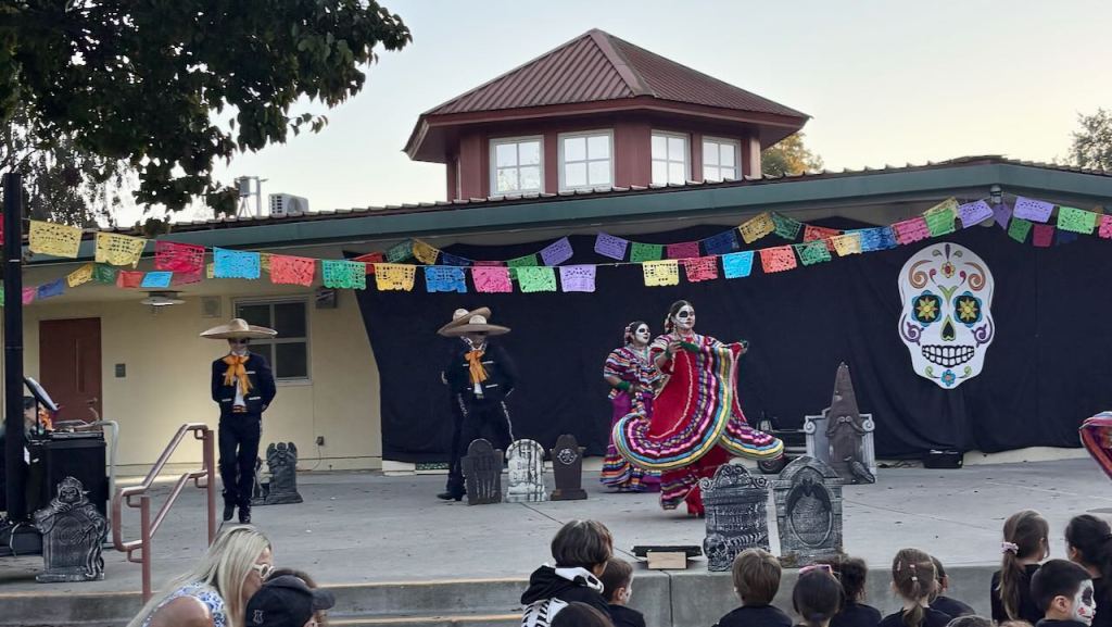 Dancers in colorful traditional dresses perform at a Día de los Muertos celebration at a Palo Alto elementary school